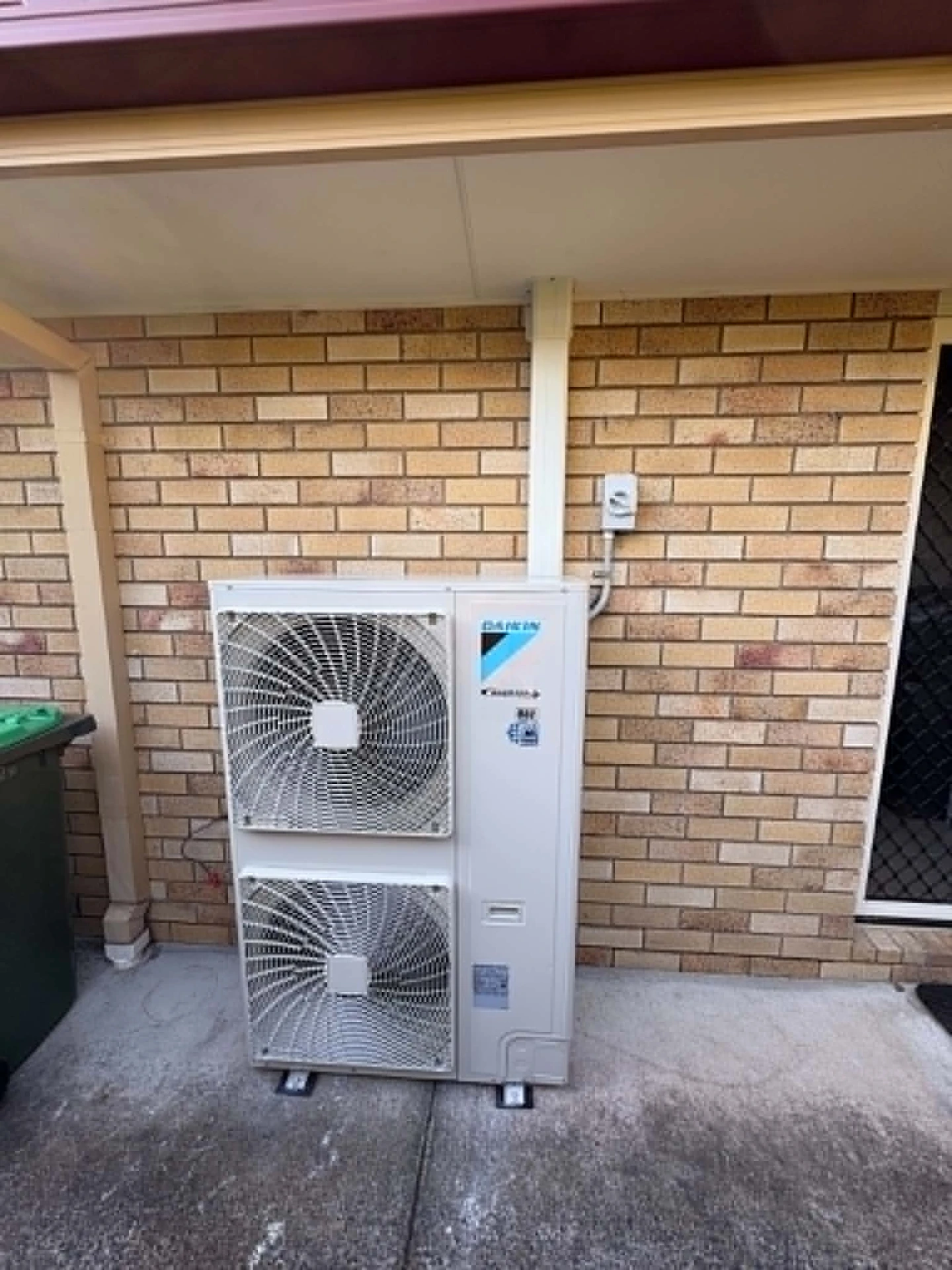 Daikin outdoor condenser unit installed against a brick wall